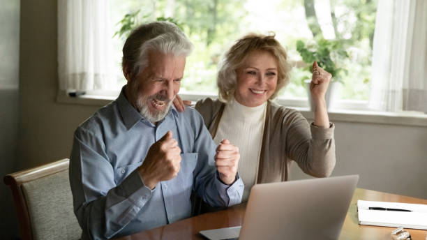 glücklich aufgeregt reifen paar feiert erfolg, blick auf laptop-bildschirm - aging process middle women men stock-fotos und bilder