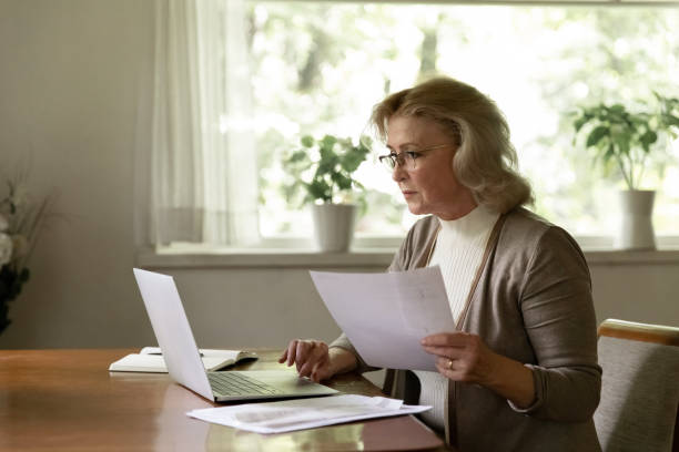 istock Focused middle aged woman holding document and using laptop 1305360058
