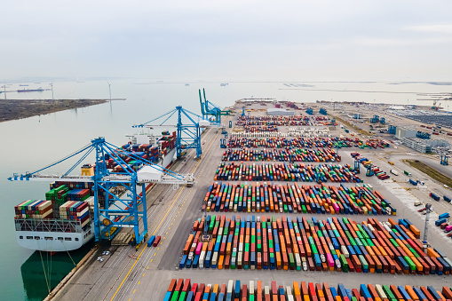 Container port with large ship being loaded and unloaded with gantry crane. International shipment and global freight transport and commerce. Aerial view of cargo harbor wharf.