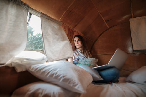 Young woman with laptop inside a motor home A young woman with a laptop while sitting on a vintage motor home bed digital nomad stock pictures, royalty-free photos & images