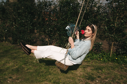 A young woman hodling a flower bouquet, in motion on a swing