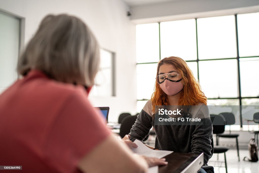 Teacher grading tests and talking to student - wearing face mask Student Stock Photo