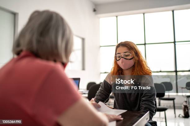 Teacher Grading Tests And Talking To Student Wearing Face Mask Stock Photo - Download Image Now