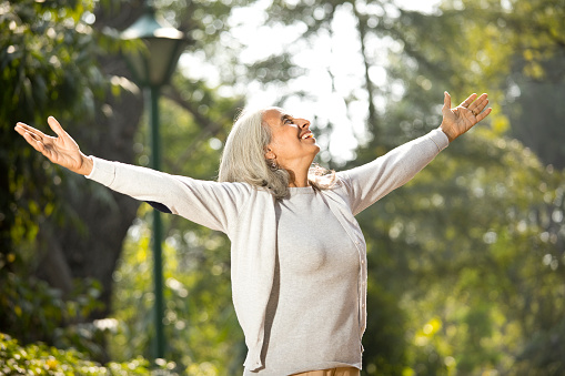Happy senior woman standing with arms outstretched at park