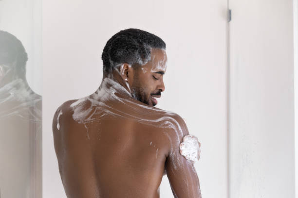 Smiling millennial african ethnicity biracial naked man taking shower. Back rear view smiling millennial african ethnicity biracial naked man cleaning exfoliating body with foamy gel, enjoying morning showering in bathroom, personal hygienic procedure routine concept. shower gel stock pictures, royalty-free photos & images