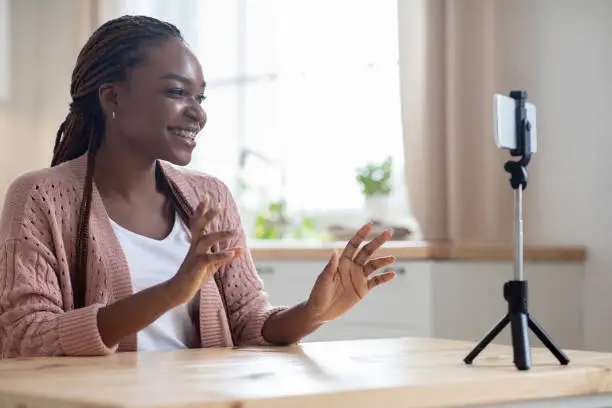 Photo of Young african american female blogger recording new video on smartphone at home