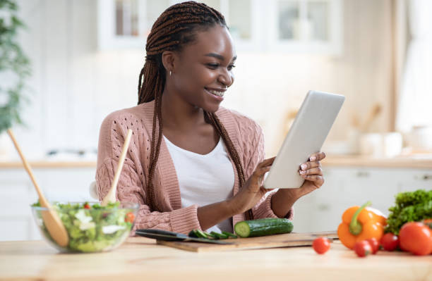 istock Online Recipe. Cheerful african woman using digital tablet in kitchen while cooking 1305367393