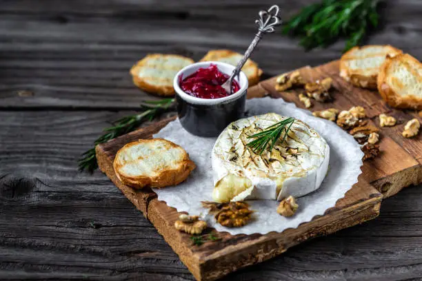 Baked camembert with toasts, rosemary, cranberries and nuts on rustic wooden table. Gourmet traditional Breakfast close up.