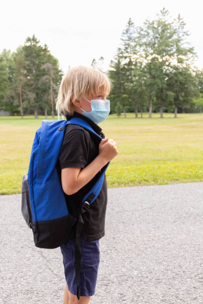 istock Child in mask with blue backpack at the school yard during corona virus. 1305371565