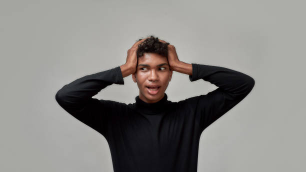 istock Amazed young guy looking aside, standing with open mouth and holding his head in surprise, posing isolated over gray background 1305373385