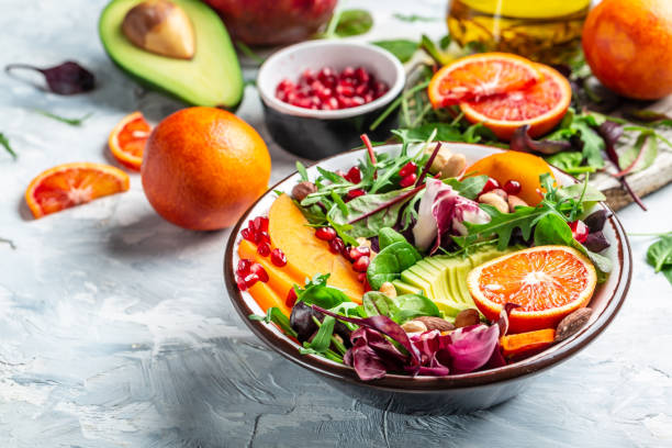 istock Healthy vegetable buddha bowl lunch with avocado, persimmon, blood orange, nuts, spinach, arugula and pomegranate on a light background, top view 1305374295