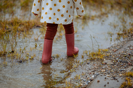 Little girl wearing pink rubber boots playing outside in the mud on a rainy day, splashing