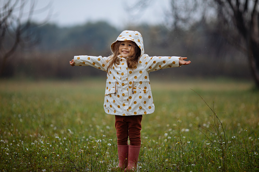 Little girl wearing pink rubber boots playing outside in the mud on a rainy day, splashing