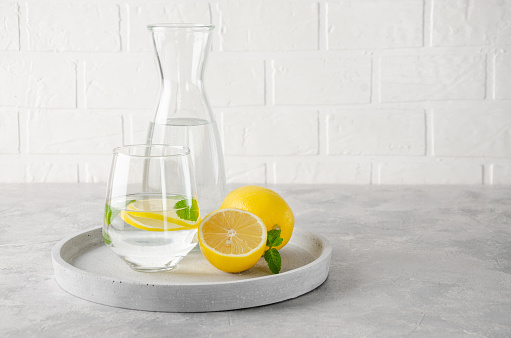 Lemon water with fresh lemons and mint leaves on a gray concrete background. A healthy drink. Copy space
