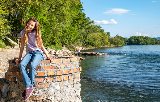 Happy cute small girl sitting at the riverbank