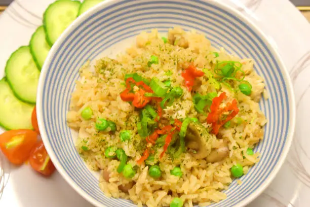 Photo of Chicken fried rice with mushrooms, green pea and seasonings with red chilli,  side dishes with organic fresh cucumber and tomatoes. Thai food.