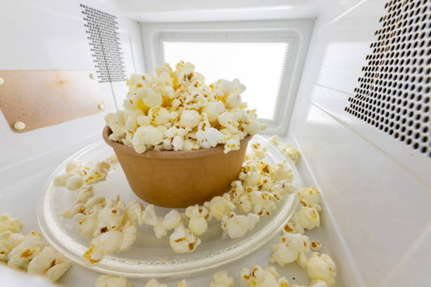 Spilled popcorn in the microwave. Salty snack prepared in the kitchen appliance. Light background. Spilled popcorn in the microwave. Salty snack prepared in the kitchen appliance. Light background. inside microwave stock pictures, royalty-free photos & images