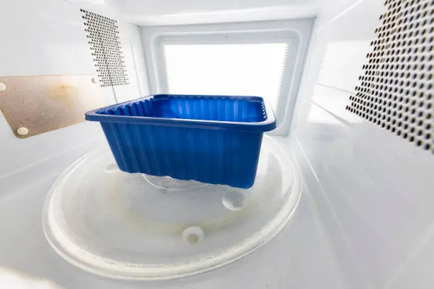 Photo of Plastic food container in a microwave oven. Preparing meals in the household. Light background.