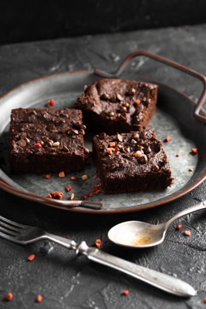 istock Dark cacao brownies with choco drops on old metal tray with vintage silverware on dark concrete background 1305384218