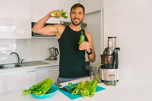 Attractive athletic active sportive man making fresh detox homemade celery juice in juicer machine at home in kitchen. Exercise and eating healthy. Detox diet for fitness. High quality photo