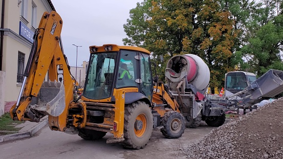 Road construction works using heavy machinery. Excavator and rotating concrete mixer near gravel and asphalt heap. Lviv, Ukraine, 03 04 2021