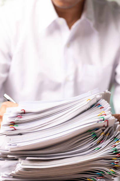 istock Vertical male office workers with white shirt holding and writing documents on office desk, Stack of business overload paper. 1305389286
