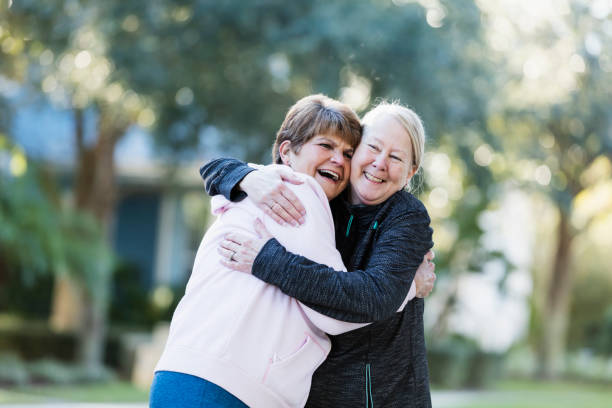 Two senior women, friends greeting each other outdoors Two senior women in their 60s, best friends, greet each other with a warm hug. They are outdoors in a residential neighborhood. cheek to cheek photos stock pictures, royalty-free photos & images