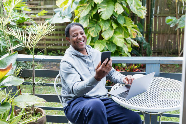 Mature black man using laptop and smart phone on patio