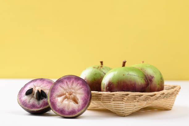 Ripe Star apple fruit (chrysophyllum cainito) Ripe purple and green star apple fruit in a bamboo basket on white and yellow background, Tropical fruit chrysophyllum cainito stock pictures, royalty-free photos & images