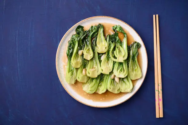 Stir fried bok choy with soy sauce on plate and chopsticks on blue background, Asian vegan food, Top view