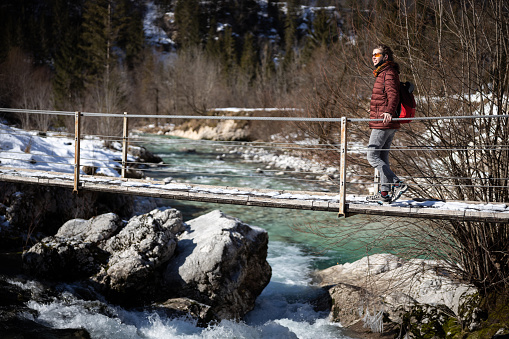 Adult woman hiking with serenity over a wooden bridge in winter.