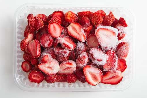 Sliced halves red berries. Plastic containers with fresh frozen strawberries