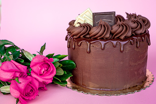 Exquisite Valentine's Day chocolate cake decorated with chocolate chips and chocolate frosting on top with flowers on the side with pink background.