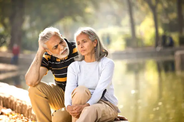 Senior man consoling his angry wife sitting at lakeshore
