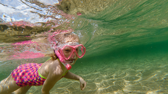 Underwater photo of a girl snorkeling, she is giving a thumbs up and enjoying her summer vacation