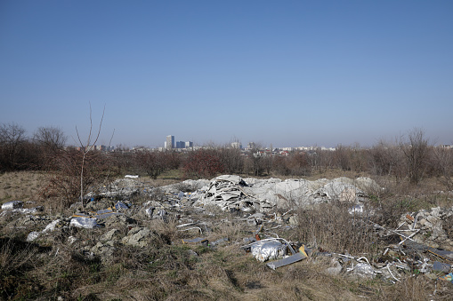 Shallow depth of field details of garbage and construction debris scattered all around an empty lot in Bucharest, near a makeshift shelter.
