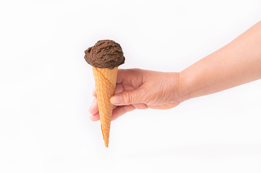 Female hand holding a tempting wafer ice cream cone with a chocolate scoop on a light background. Close up. Ice cream and lifestyle concept.