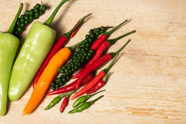 Group of various fresh pepper varieties on wooden chopping board background, copy space