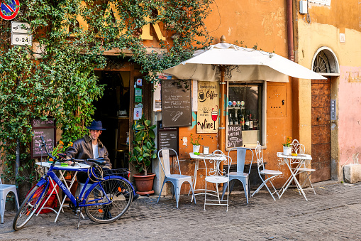Rome, Italy, March 03 -- A young adult enjoying a good book sitting in a picturesque and trendy café in Trastevere, in the historic center of Rome. Trastevere is one of the most iconic district of the eternal city, for the presence of monuments and ancient churches, but also for small squares and alleys where it is easy to find typical restaurants, pubs and little store. Image in High Definition Format.