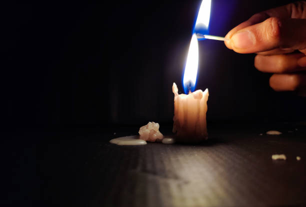 Stock photo of a human hand holding lighted matchsticks with yellow and blue color flame for lighting up the white color small candle on black dark background. focus on object. stock photo