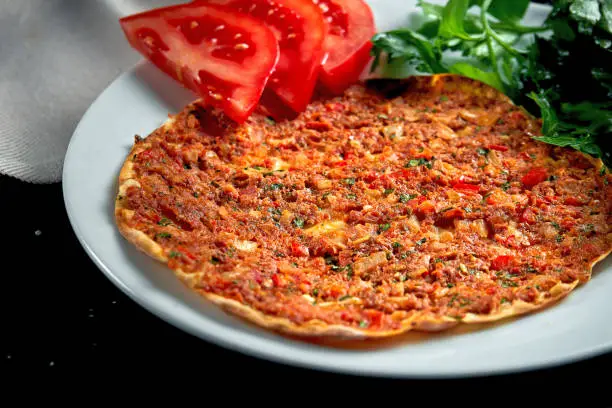 Lahmacun is a popular Turkish dish. Thin crispy tortilla with minced lamb, tomatoes and bell pepper on black background