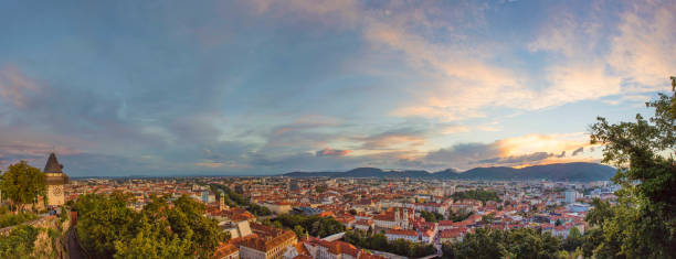 paysage urbain de graz et la tour de l’horloge (grazer uhrturm), célèbre attraction touristique sur la colline du shlossberg, graz, région de styrie, autriche, au coucher du soleil. ciel dramatique, vue panoramique - graz clock tower clock austria photos et images de collection