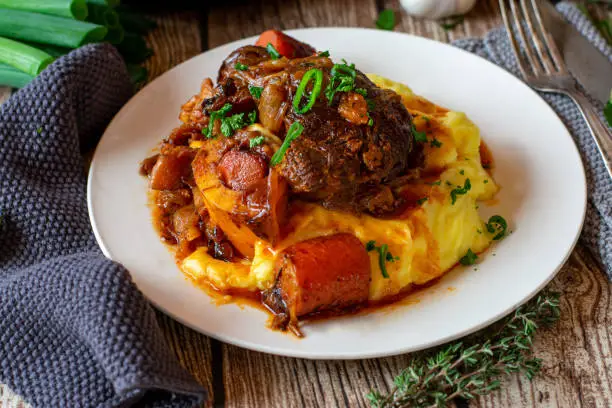 fresh braised beef shanks with mashed potatoes, delicious gravy and vegetables such as carrots and onions served on a plate. Traditional ossobuco meal