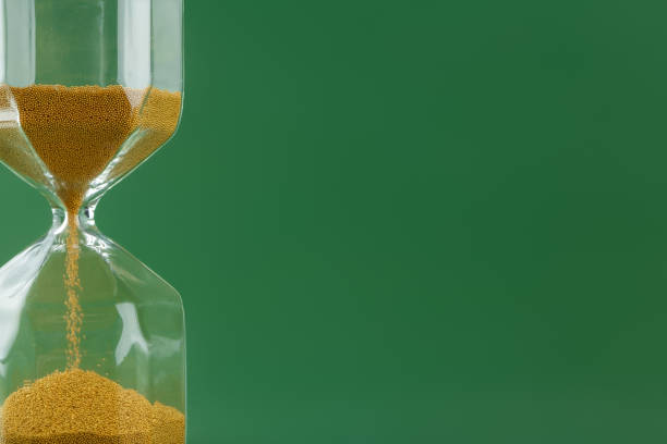 istock Gold hourglass on dark green paper background 1305446443
