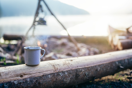 A white tea cup in front of campfire and beautiful view of lake.