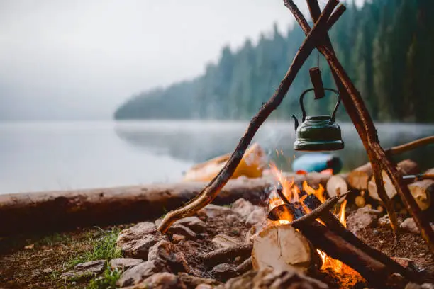 Campfire with a vintage kettle next to the beautiful lake.