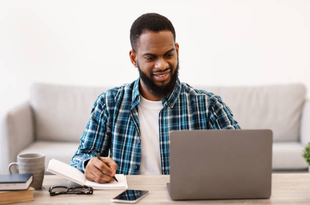 istock Cheerful African Businessman Taking Notes Working On Laptop In Office 1305453757