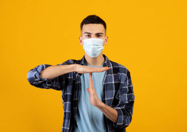 istock Stop covid-19. Caucasian guy wearing protective face mask, gesturing STOP or TIME OUT to camera on orange background 1305455313