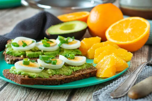 open Sandwiches with avocado and boiled eggs served on a bamboo plate with fresh fileted oranges