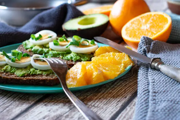open Sandwiches with avocado and boiled eggs served on a bamboo plate with fresh fileted oranges